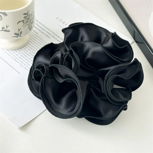 Detailed view of a large black satin scrunchie with ruffled edges and silky texture