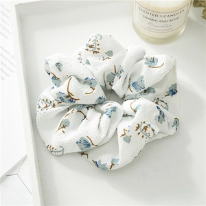 Detailed texture of ruffled white scrunchie with blue floral print on wooden tray