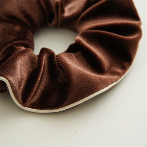 Close-up of brown velvet scrunchie with white piped edges and soft textured folds