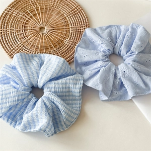Detail view of light blue checkered and daisy embroidered scrunchies on a woven mat