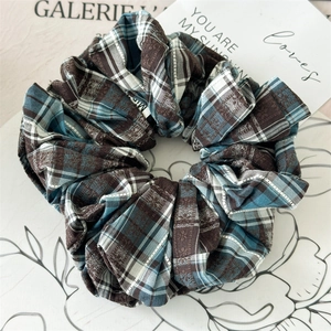 Detailed view of oversized plaid scrunchie in brown and blue tones on white ceramic plate