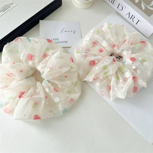 Detail view of two large mesh hair scrunchies with colorful polka dots on a desk
