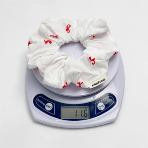 Détail d'un chouchou blanc avec motifs de nœuds rouges pesant 11,6 g sur une balance