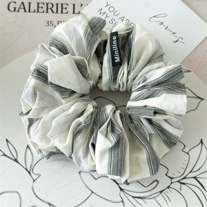 Detail of grey striped fabric scrunchie with Miniline woven label on a minimalist background