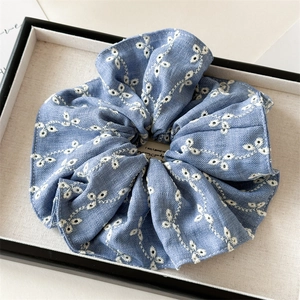 Detailed view of blue denim hair scrunchie with white floral embroidery and fine stitching