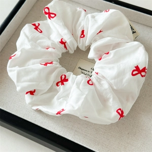 Détail d'un chouchou blanc avec motifs de nœuds rouges sur tissu en coton plissé