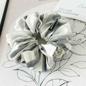 Close-up of pleated grey striped fabric scrunchie with brand label and minimalist card