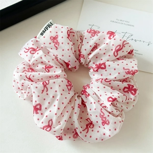 Détail d'un chouchou en mousseline blanche avec motifs de nœuds rouges et étiquette de marque