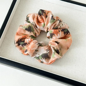 Gros plan sur chouchou en mousseline florale avec motif tie-dye rose orange sur plateau
