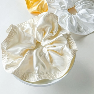 Macro detail of glossy satin scrunchies in cream and yellow with elegant ruffled texture