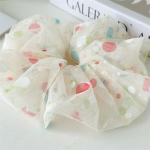 Detailed texture of off-white mesh scrunchie with colorful polka dots on a minimalist table