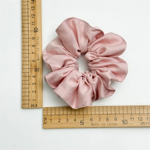 Chouchou en coton tencel rose mesuré avec des règles sur un fond blanc neutre