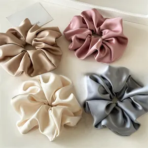 Detailed view of four satin jumbo hair scrunchies in champagne, pink, white, and blue colors