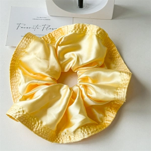 Detailed close-up of bright yellow satin scrunchie showing glossy texture and ruffle edges
