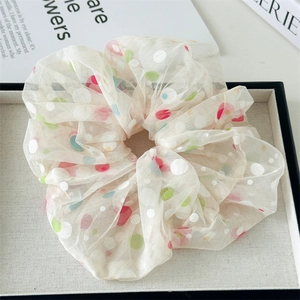 Detailed close-up of a large mesh hair scrunchie with colorful polka dots on a display tray