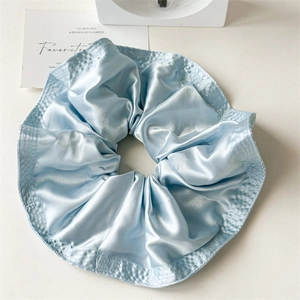 Detail view of light blue satin scrunchie with neat stitching and pleated fabric texture