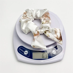 Close-up of floral satin bow hair scrunchie weighing 6.3g on a scale showing lightweight material