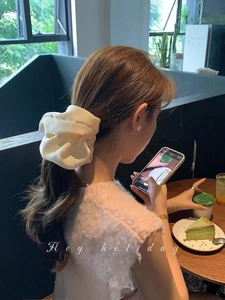 Close-up of a cream oversized satin scrunchie with rich pleats styling a low ponytail
