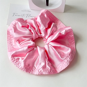Macro shot of large pink satin scrunchie showing detailed pleated texture and fine stitching