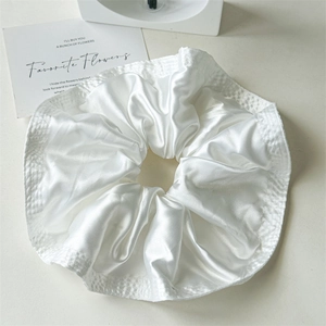 Macro detail of white satin scrunchie showing glossy fabric texture and ruffled edges