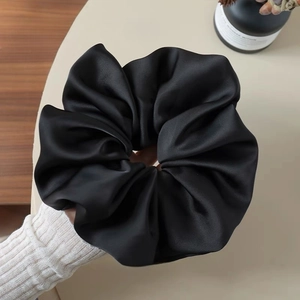 Detailopname van een oversized zwarte satijnen scrunchie met een zijdezachte glans