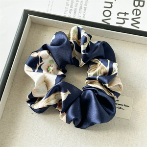 Detailed close-up of floral satin scrunchie with soft silk luster on a grey tray
