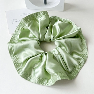 Detailed view of light green satin scrunchie with layered pleats and reinforced stitching