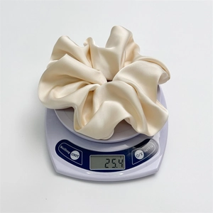 Detail view of a large champagne satin scrunchie on a scale weighing 25.4 grams