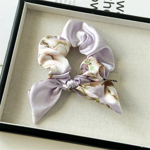 Detail of floral satin scrunchie with long bow tail on beige textured tray
