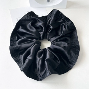 Close-up of elegant black satin oversized scrunchie with glossy texture and ruffles
