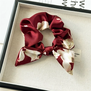 Detail of burgundy satin floral scrunchie with elegant bow on a textured linen tray