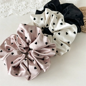 Detailed close-up of three satin scrunchies with elegant heart patterns and silk texture