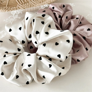 Close-up of cream and dusty pink satin scrunchies with black heart patterns on lace