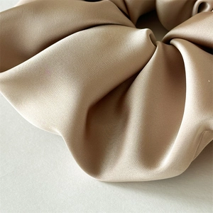 Macro shot of large satin scrunchie in champagne gold showing soft fabric texture