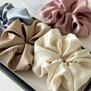 Close-up of oversized satin scrunchies in soft Morandi colors on a textile tray
