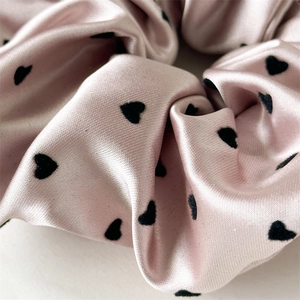 Close-up of pink satin scrunchie featuring elegant black heart patterns and silky texture