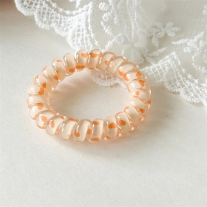 Détail d'un chouchou spirale beige avec des motifs cœurs orange sur dentelle blanche