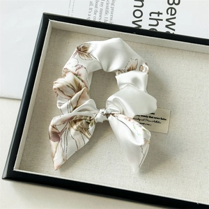 Detail of ivory satin floral scrunchie with bow tie on a textured display tray