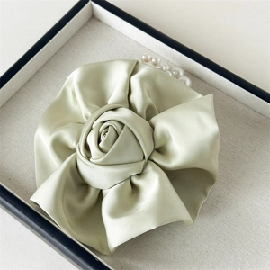 Détail d'un chouchou rose en satin vert clair avec perles blanches élégantes et texture soie