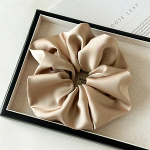 Detailed view of a champagne satin scrunchie on a display tray with elegant fabric texture