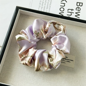 Close-up of lilac floral satin scrunchie with silky texture on a display tray