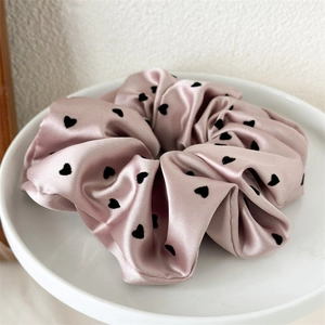 Detail of elegant dusty pink satin scrunchie with black heart pattern on a ceramic plate