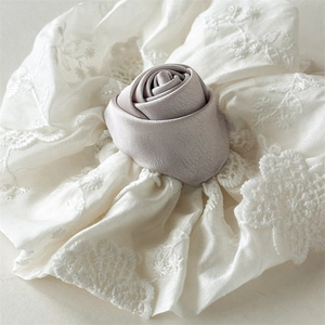 Vue détaillée du chouchou en dentelle crème orné d'une rose en tissu de couleur lilas