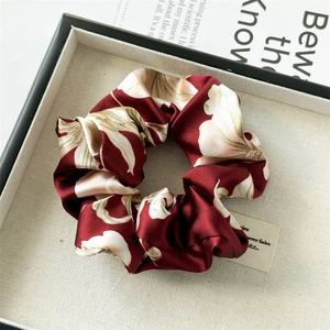Macro detail of wine red floral satin scrunchie displayed in a texture gift box
