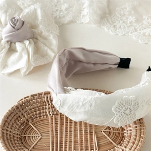 Détail d'un serre-tête en dentelle crème et chouchou rose sur un panier tressé