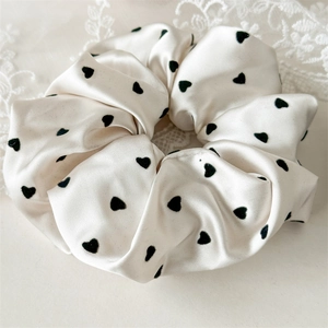 Detail of elegant cream satin scrunchie with black heart print and smooth silk texture