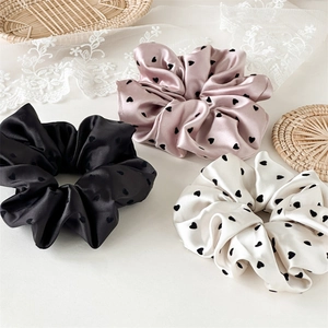 Detailed close-up of three satin scrunchies in black, pink, and white with heart patterns