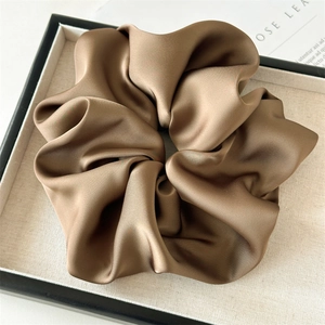 Macro detail of glossy brown satin scrunchie showing premium pleated fabric texture