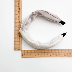Gros plan d'un serre-tête en satin gris torsadé et dentelle blanche avec règle en bois
