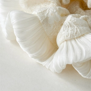 Détail macro de la broderie en lin blanc crème et de la texture plissée de ce chouchou chic